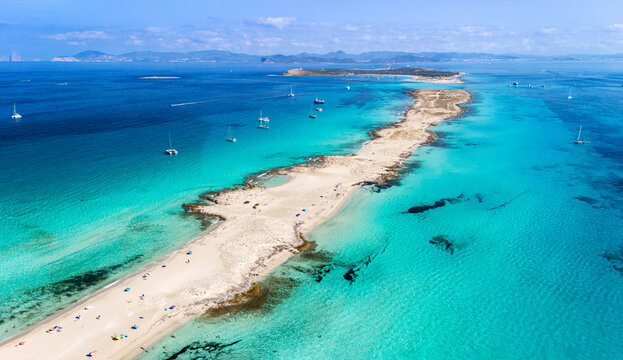 Aerial view of Formentera island in the Balearic Islands, Spain, with turquoise crystal-clear waters, sandy beaches, and boats anchored along the Mediterranean coast on a sunny summer day.