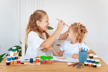 children draw with paints, two girls with painted multicolored hands laugh and indulge on a white isolated background, a place and space for text, small artists and children's creativity