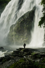 A man stands in front of a waterfall 𝙆𝙝𝙡𝙤𝙣𝙜 𝙇𝙖𝙣 waterfall , 𝙆𝙖𝙢𝙥𝙝𝙖𝙚𝙣𝙜 𝙋𝙝𝙚𝙩