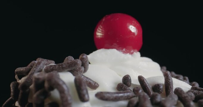 A chocolate frosted cupcake with sprinkles on top and a red cherry on top