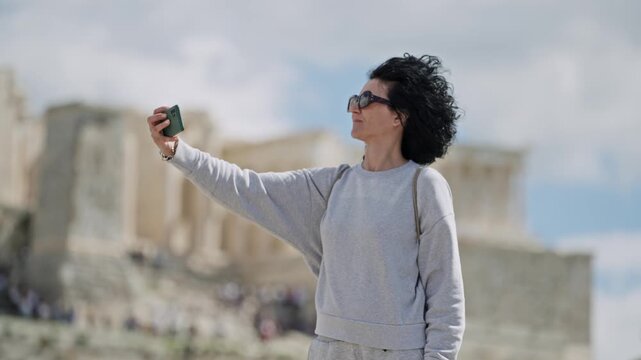 Tourist curly hair woman make selfie with smartphone at Acropolis in Athens on sunny day from Areopagus Hill