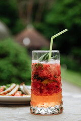 Refreshing cocktail with a straw on a table in a garden setting.