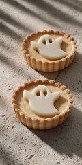 Light-toned tartlets with ghost-shaped white toppers on concrete background and soft shadows, ideal for modern Halloween food design and ads.