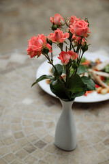 Coral roses in a white vase on a mosaic table