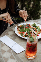Woman enjoying a fresh salad and a refreshing drink at an outdoor cafe.