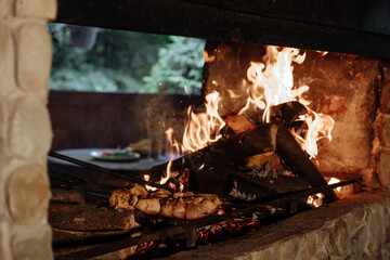 Grilled meat cooking over a roaring fire in a stone fireplace