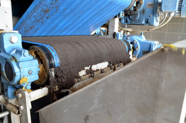 A dirty industrial belt filter press in operation, with sludge being dewatered on a moving conveyor belt, representing wastewater treatment and environmental technology.