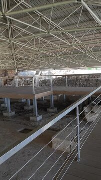 Archaeological excavation site, the Soli Basilica ruins in Cyprus, showing ancient stone foundations, protected by a modern metal truss roof and viewing platforms for visitors.