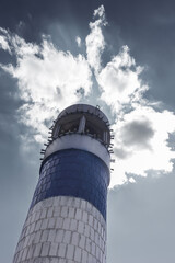 The tall lighthouse tower is made of blue and white bricks under an impressive blue cloudy sky.
