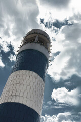 The tall lighthouse tower is made of blue and white bricks under an impressive blue cloudy sky.
