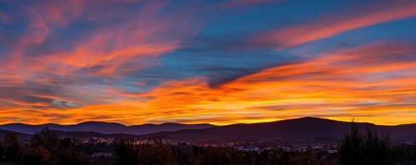 Obraz premium A vibrant sunset paints the sky with hues of orange, purple, and blue, casting a serene atmosphere over a distant landscape.