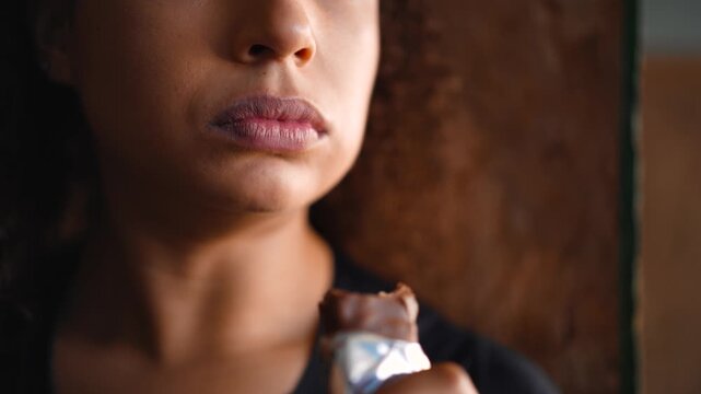 Extreme close-up of Black female athlete taking bite of chocolate protein bar showing detailed texture of nutritional supplement 