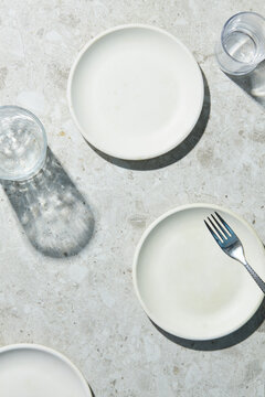 empty white plates on a grey terrazzo background with transparent glasses and a fork