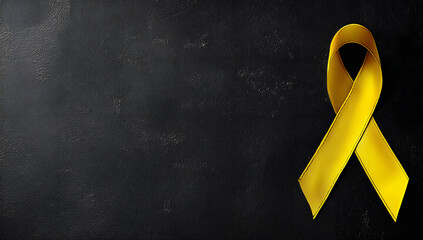 Yellow ribbon on black background, symbolizing cancer awareness and support with copy space for health campaigns and title banners
