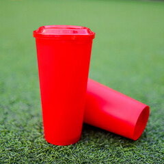 Vibrant Red Cups on Green: Two bold, red cups rest on a bed of fresh, vibrant green grass,...