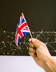 Hand holding a small Union Jack flag against a black background with a light design
