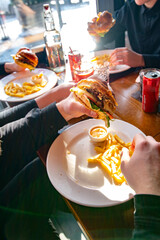 Unrecognizable friends eat burgers and fries at the table in a fast food restaurant