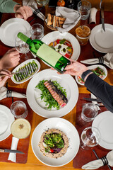 Unrecognizable Group of friends eat at a set table in a restaurant while the waiter pours wine. Top view
