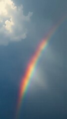 A vibrant rainbow appears in a cloudy sky with sunlight shining through the clouds.
