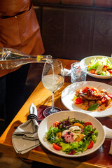 Unrecognizable Waiter pours wine into a glass on a table served with food in a restaurant