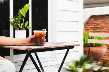 Woman hand holding glass iced coffee on table outside.