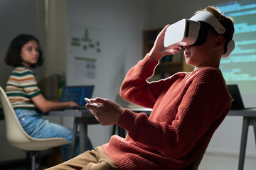 Caucasian teenage boy wearing virtual reality headset interacting with controller while sitting in...
