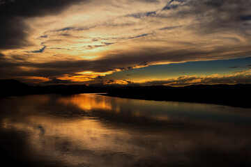 Obraz premium A breathtaking sunset after rainfall in Mongolia, where dramatic clouds glow in fiery red and deep blue hues. The sun sets like burning fire behind the horizon, casting mountains and trees in striking