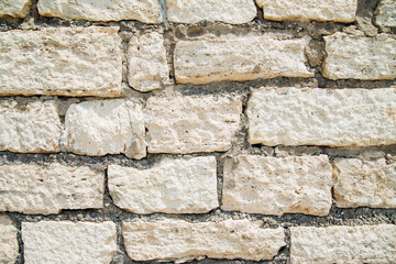 Textured wall of rectangular stone blocks in light beige shades and cement between them.