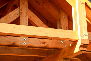 Warm sunlight bathes an intricately crafted wooden roof structure, where exposed beams and sturdy bolts showcase natural wood textures. 