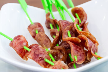 Sliced Chinese sausage skewers on green sticks, ready for grilling or serving as a savory appetizer.