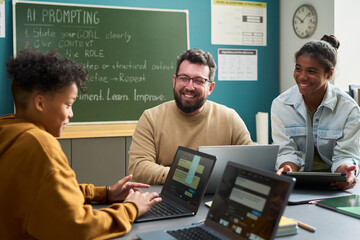 Caucasian man smiling and interacting with Black teenage girl and Black teenage boy using laptops...