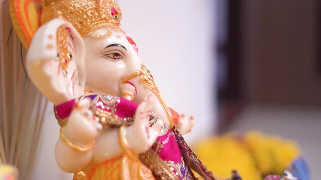 Beautifully decorated white marble Lord Ganesha (Ganpati) idol in close-up, with a flickering diya for Ganesh Chaturthi or Diwali puja