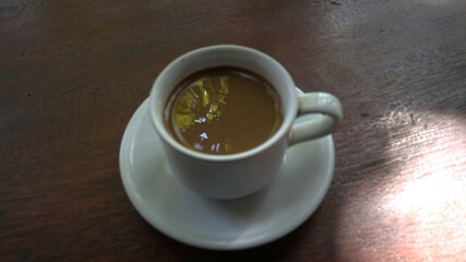 A steaming mug of coffee rests on a wooden table with natural light streaming in