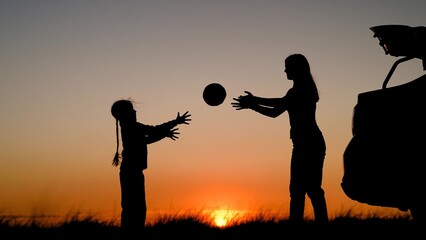 Parent child daughter stopped at camping by car. Happy mom kid playing with ball in nature near car. Family traveling by car mom child girl. Mother child girl travel by car, play on field, sunset sky