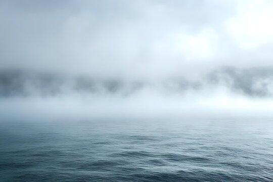 Atmospheric seascape with dense fog hovering over calm ocean waters creating mysterious moody scenery in cool blue tones, dramatic minimalist nature background.