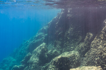 Sunbeams filter through the deep blue ocean to illuminate a majestic underwater cliff. Serene marine seascape background.