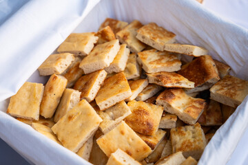 A basket lined with cloth holds neatly cut cubes of pastry, offering a rustic and inviting display of fresh baked treats on a natural setting.