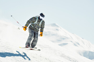 Skier performing aerial jump trick on snowy mountain slope during winter holiday adventure in alpine ski resort under clear blue sky