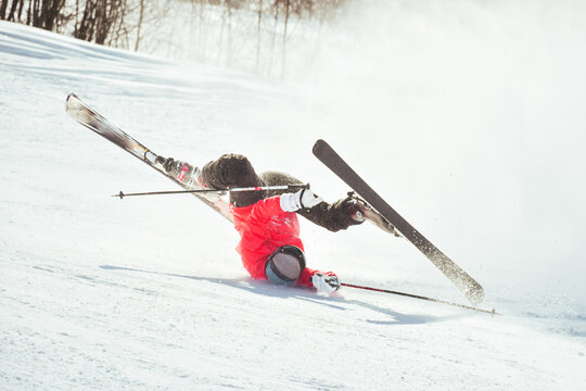 Skier fall down hit head painfully on hard groomed piste with snow swirls on ski resort slope. Sports Injury young skier in professional sports concept.. Reckless