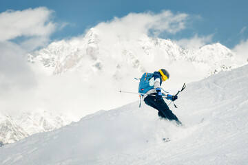 Playful Skier performing switch skiing trick backwards on snowy slope with mountains in background