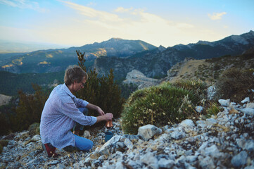 Naklejka premium Man Cooking with Portable Stove on Scenic Mountain Landscape at Sunset