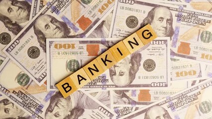 Wooden blocks with the letters "Banking" arranged on a slowly rotating stack of dollar bills. Looping 360-degree of wooden blocks with the words "Banking" as a business financial concept. 4K. - Powered by Adobe