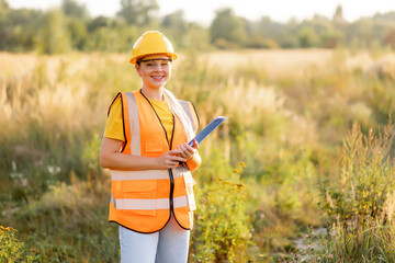 Smiling female engineer inspecting a field wearing a safety vest and helmet