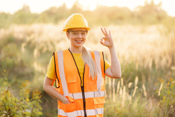 Female construction worker gesturing okay sign in a field during sunrise