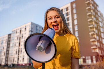 Smiling woman with a megaphone standing in front of modern residential buildings