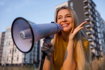 Joyful woman using a megaphone outdoors with modern buildings in the background