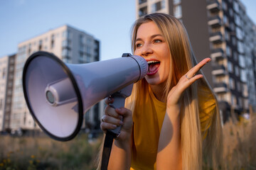 Cheerful woman outdoors using megaphone during a sunny day near buildings.