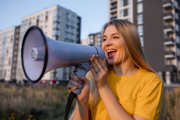 Smiling woman with a megaphone outdoors near modern apartment buildings