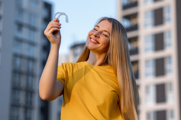 Smiling woman holding a clear dental aligner in an urban setting