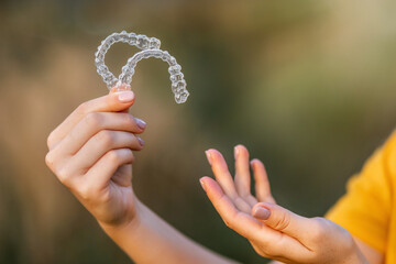 Close-up of hands holding clear teeth aligners in natural outdoor setting